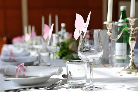 Weiß-rosa gedeckter Hochzeitstisch mit rosanen Schmetterlingsdekor an den Gläsern
